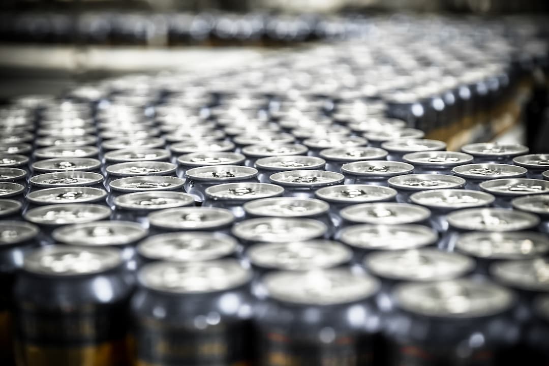 Eine Reihe von Bierdosen, die sich in einer Produktionsanlage entlang eines Förderbands bewegen und den Prozess der Dosenherstellung darstellen.